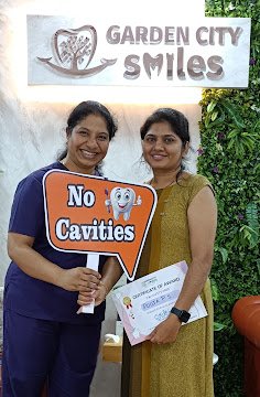 A visitor and clinician holding a No Cavities sign
