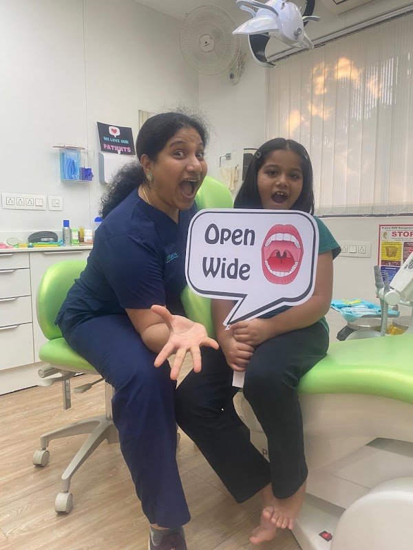 A child and clinician with an Open Wide sign beside the dental chair