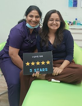A visitor and clinician holding a five-star sign beside the dental chair