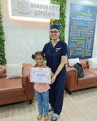 A child holding a certificate beside a GardenCity Smiles team member.